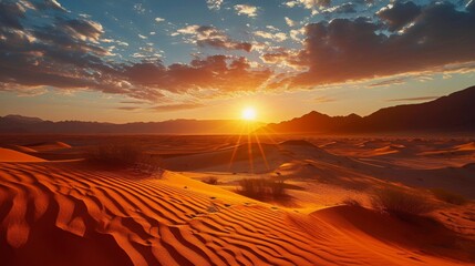 The sun is set over a desert with sand dunes and mountains with a few clouds in the sky.
