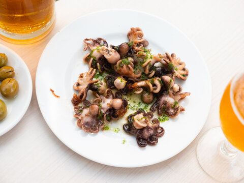 Delicious baby octopuses (Pulpitos) on plate with herbs in restaurant