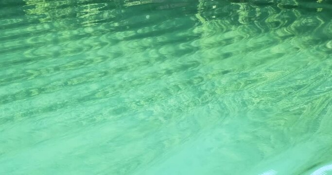 Bright turquoise water of mountain lake, close up. Beautiful abstract ripples, green forest reflected on river surface. Fresh ecology of untouched reserve nature. Natural water texture in slow motion