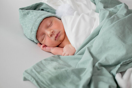 A 3-day-old baby wrapped in white cloth sleeping on a white background