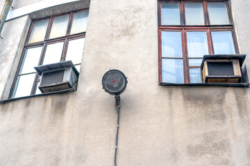 Gray old wall with a lantern in the middle and two windows, view from below.