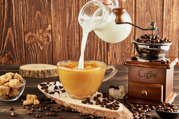 Pouring coffee from glass jug milk into glass cup with coffee, vintage coffee grinder and lump...