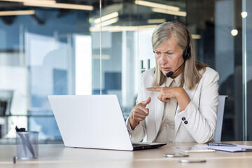 A serious and focused senior business woman conducts an online video meeting with clients and...