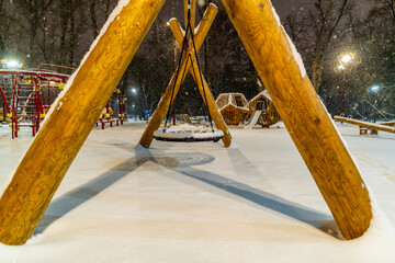 Children's round swing in the park under the snow on a winter evening.