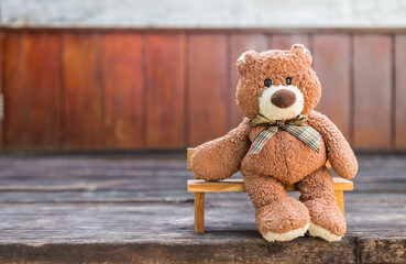 Brown teddy bear sitting on wooden bench with space on wooden wall background, outdoor day light