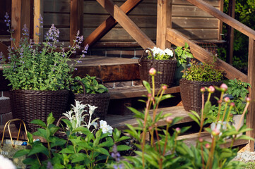 wooden rustic front house porch decorated with flower pots with flowerbed on foreground.