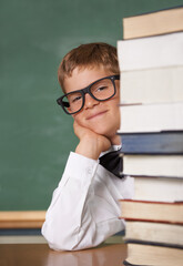 Child, school portrait and stack of books for education, language learning and knowledge in classroom. Happy face of kid, boy or student in glasses with textbook, literature and library resources
