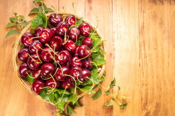 Sweet Red cherry in bamboo basket on wooden background, Red cherry with leaf on table.