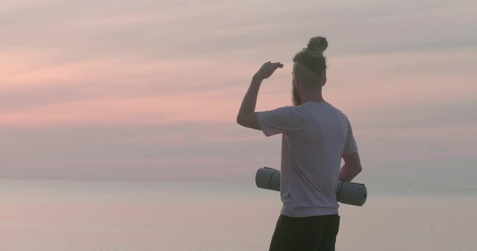 Solitary contemplation back view of man with exercise mat in hand looking at ocean. Solitary contemplation journey into big inner world Solitary contemplation seeking harmony in nature.