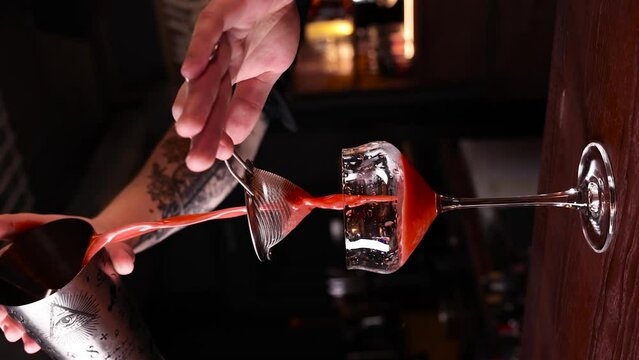 a red cocktail is poured into a glass alcohol wine juice  making a cocktail at the bar vertical video