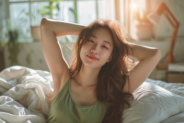 An attractive Asian woman wearing green casual clothes stretches after waking up in bed. Lazy girl activities on Sunday morning