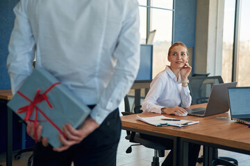 Holding gift box for woman. Two employees are working in the office