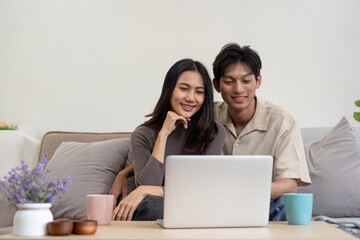 Young couple asian using laptop together while sitting on sofa at home