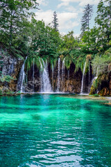 Low angle view of multiple waterfalls streaming into a beautiful, tranquil, clear lake at Plitvice...