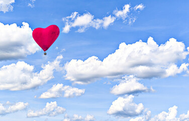 Red heart-shaped hot air balloon flying over a blue sky with white clouds	