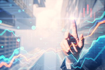 Close up of businessman hand pointing at glowing forex chart on blurry bright city backdrop. Trade,...