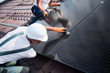 Workers building photovoltaic solar panel system on rooftop of house. Close up of men technicians...
