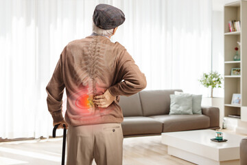 Older man with a cane standing in a living room and holding his painful back