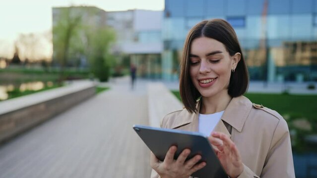 Young, Smiling, and Attractive Woman Outside Using Tablet, Chatting on Social Media with Colleagues.