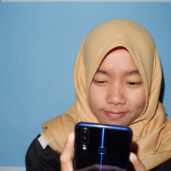 An Asian woman wearing a headscarf is playing a smart phone.