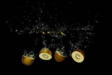 Four pieces of sliced kiwis falling into water with a black background creating bubbles and a splash
