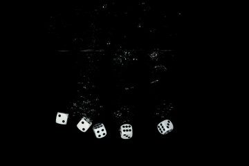 Five black and white dices falling into water with a black background creating bubbles and a splash
