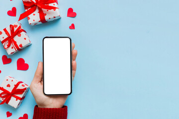 Woman hand holding mobile phone with blank screen on colored background with hearts, valentine day concept top view flat lay