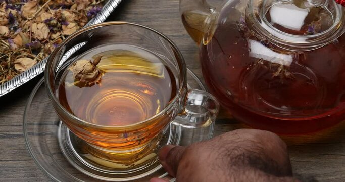 Make mix pour herbal floral tea drink transparent glass teapot to teacup twister pick up put rustic wooden table