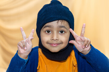 An Asian boy wearing a monkey cap is showing the V sign with the fingers of both hands.