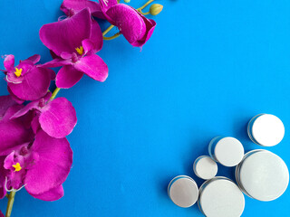 Purple Orchid Flowers and Silver Cosmetic Jars on Blue Background