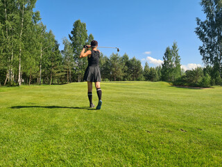 Graceful Golfer Swings on a Picturesque Golf Course Surrounded by Trees Under Clear Blue Sky