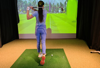 Woman practicing golf swing in modern indoor facility with golf simulator and large screen display