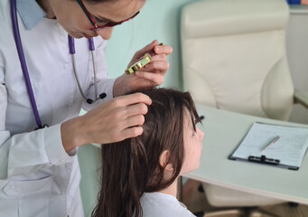 Female doctor examining childs scalp for lice or nits with a magnifying glass in a medical clinic - obrazy, fototapety, plakaty