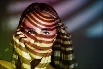 Woman, art and portrait with creative, lights and pattern projection with cosmetics and beauty. Shadow, confidence and female model with makeup, serious and spotlight with retro fantasy in studio