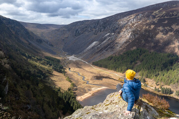 Fototapeta na wymiar mountaineer sitting on a rock, looking at landscape of Wicklow mountains, ireland