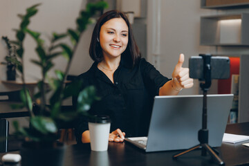 Happy young woman drinks coffee from paper cup and works at computer in cafe, modern workplace and fast life concept