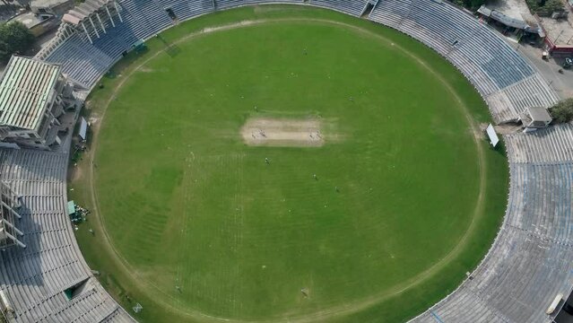 Drone zoom out shot of players playing cricket in stadium of Gujranwala during daytime in Punjab, Pakistan.