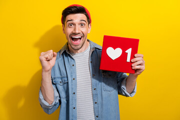 Photo of funky lucky guy wear denim jacket rising fist showing positive heart like card isolated yellow color background