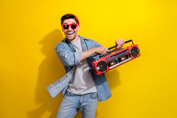Naklejka premium Photo of funny cheerful guy wear denim jacket dark glasses enjoying boom box music isolated yellow color background