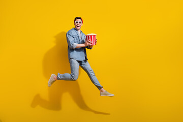 Fototapeta na wymiar Full length photo of cheerful cool man dressed jeans shirt eating pop corn watching vr movie empty space isolated yellow color background