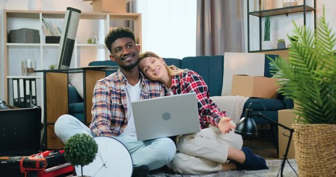 Woman putting her head on man shoulder and they together talking about design interior of their new apartment using scheme on laptop