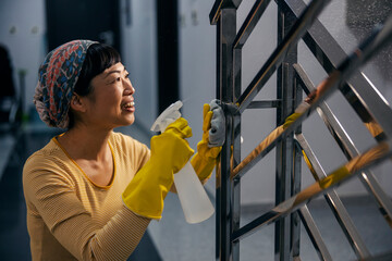 A middle-aged japanese maid is cleaning banister on stairs in building hallway.
