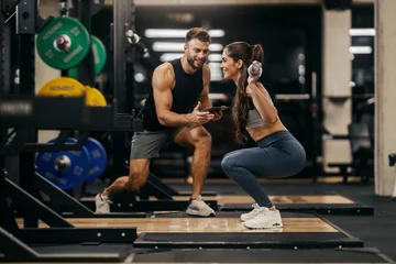 Fotobehang Persoonlijk Side view of a sportswoman lifting bar in a gym with personal trainer support.  © Dusan Petkovic