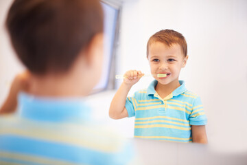 Boy child, brushing teeth and mirror in bathroom for cleaning, hygiene or health for routine in home. Kid, toothbrush or reflection for dental wellness, smile or results in morning at family house