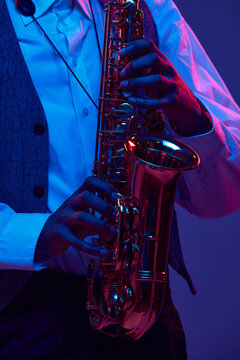 Cropped photo of African-American jazz-man playing saxophone, wind instrument against gradient background in mixed neon light. Concept of classical musical instrument, concerts and festivals. Ad