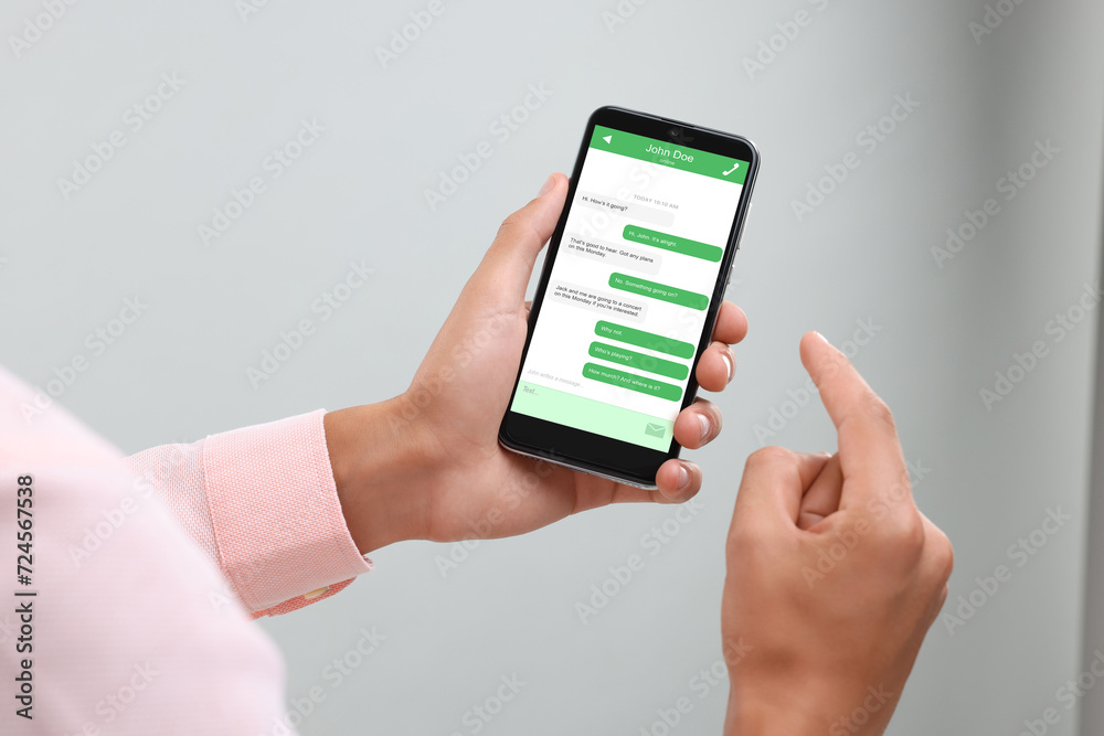 Wall mural man texting with friend using messaging application on smartphone against light grey background, clo