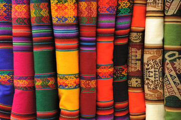Beautiful traditional Peruvian textile folded neatly and vertically, genuine aguayo fabric or tribal ethnic stripy and colorful woven clothing, blankets or rugs, displayed in at a market stall in Peru