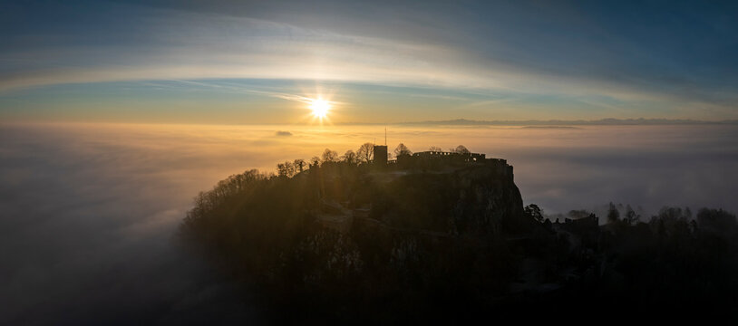 Luftbild-Panorama vom Hegauvulkan Hohentwiel mit der oberen Festungsruine als Silhouette bei Sonnenaufgang, die bei einer Inversionswetterlage aus dem Nebel herausragt