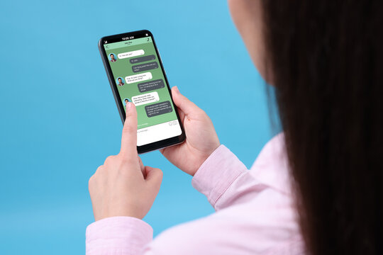 Woman texting with friend using messaging application on smartphone against light blue background, closeup