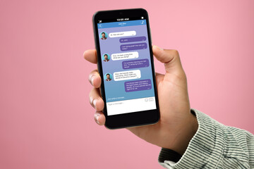 Man texting with friend using messaging application on smartphone against pink background, closeup
